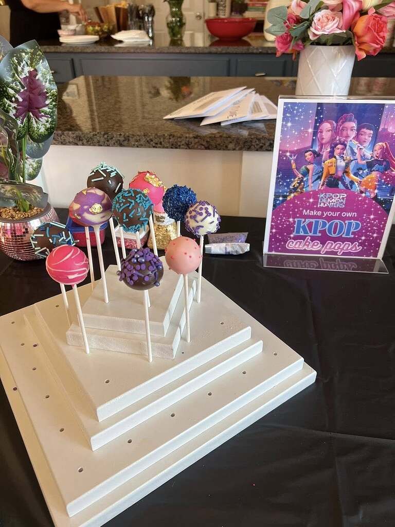 Display of colorful, decorated cake pops next to a K-Pop Demon Hunters DIY activity sign