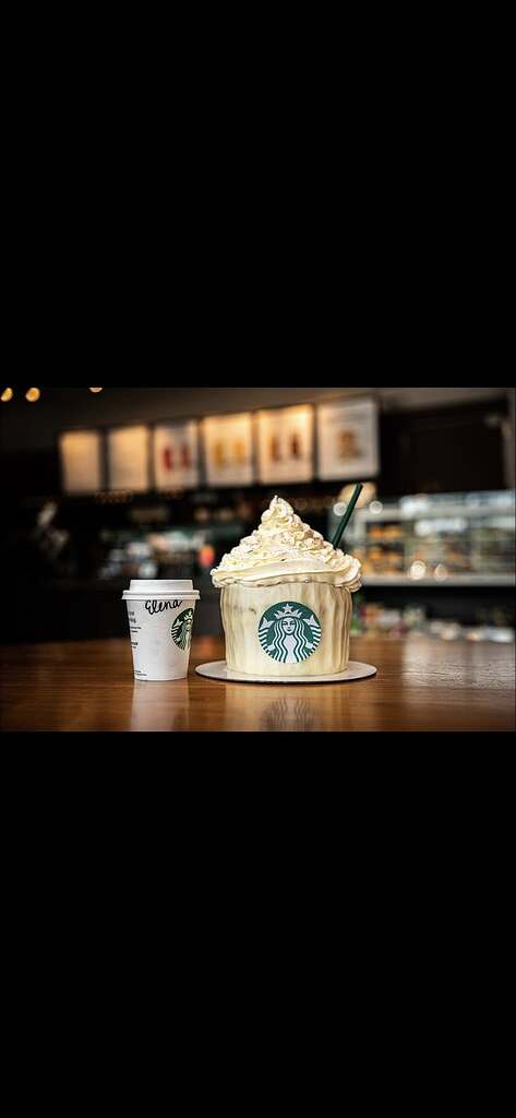 Starbucks cup-shaped cupcake with whipped cream frosting next to a small personal coffee cup.