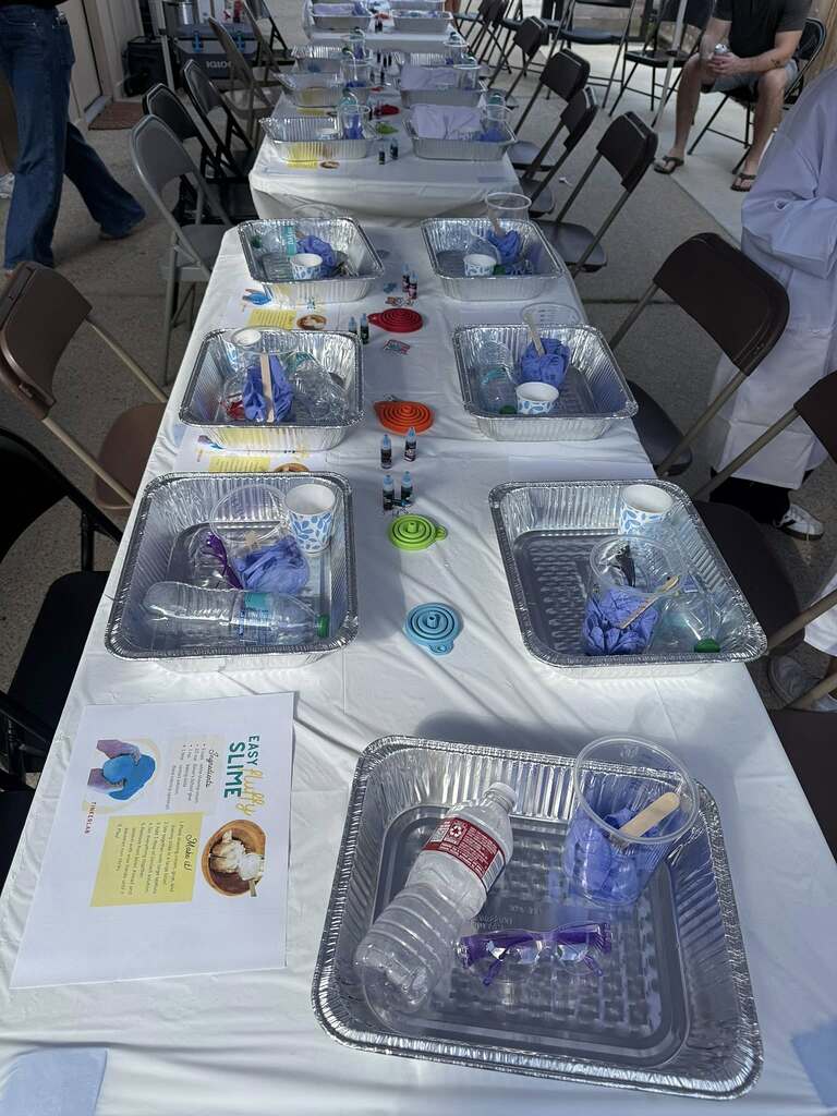 Table set up for a slime making activity with individual aluminum trays, plastic cups, and recipe cards