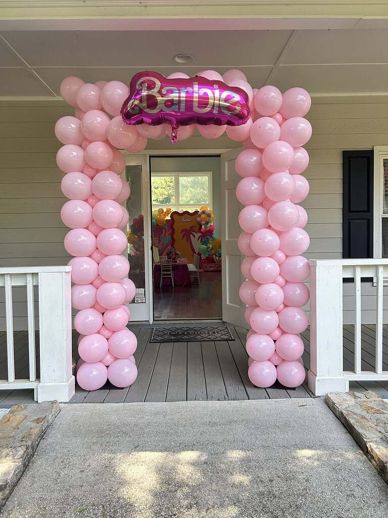 Doorway arch made of pink balloons with a Barbie foil balloon centerpiece for a themed party.