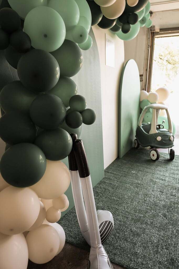 Sage green and cream balloon arch with a toy car decoration for a children's party setup.