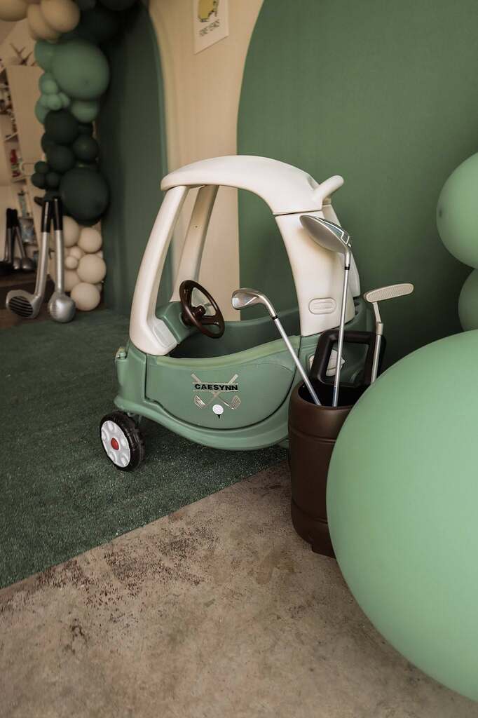 Customized green toy push car decorated for a golf-themed party with a personalized Caesynn sticker and golf clubs.